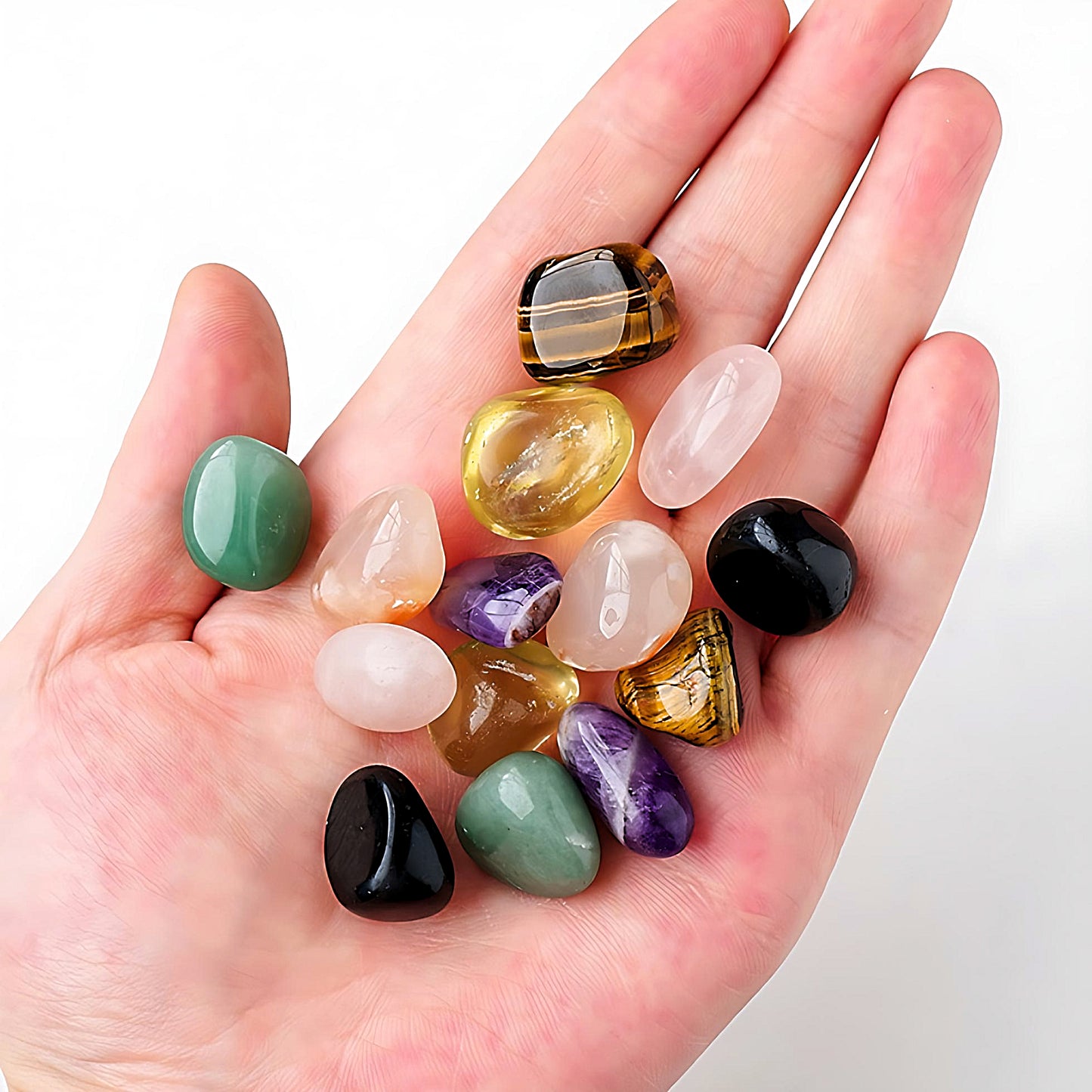 someone holding semi-precious tumbled stones: green aventurine, yellow topaz, tiger eye, pink quartz, obsidian, amethyst and flower agate